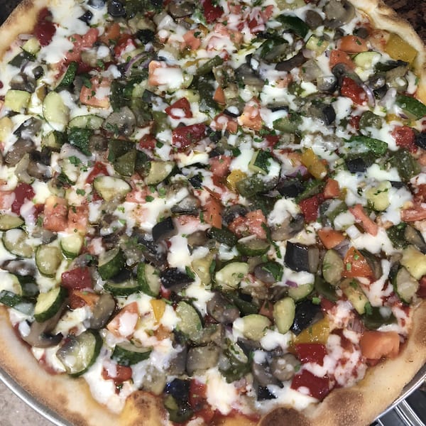 Close-up of a Fabio's Pizzeria vegetable pizza with zucchini, mushrooms, tomatoes, and melted cheese.